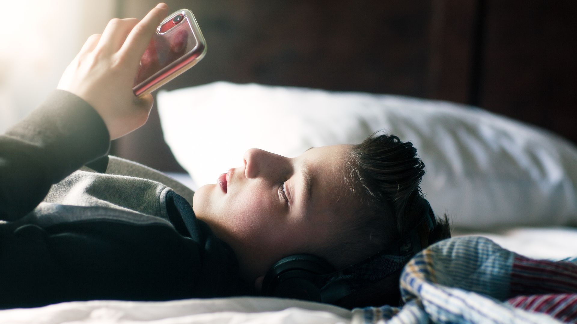 Boy lies on bed looking at his phone