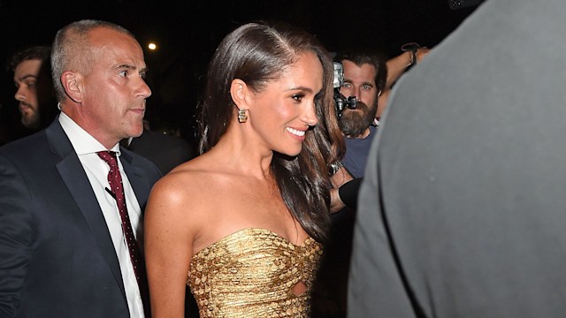 Meghan Markle wearing a gold dress and smiling as she leaves awards in New York