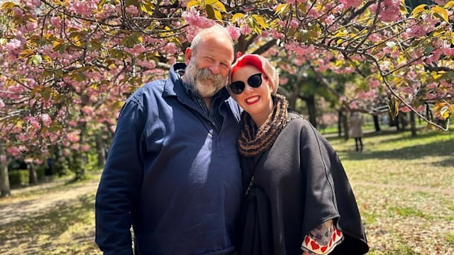 Dick and Angel Strawbridge stand side by side under a blossom tree for a photo