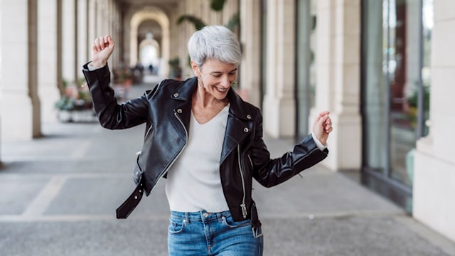 Cheerful and happy mature woman dancing in the middle of the street. Happiness concept.