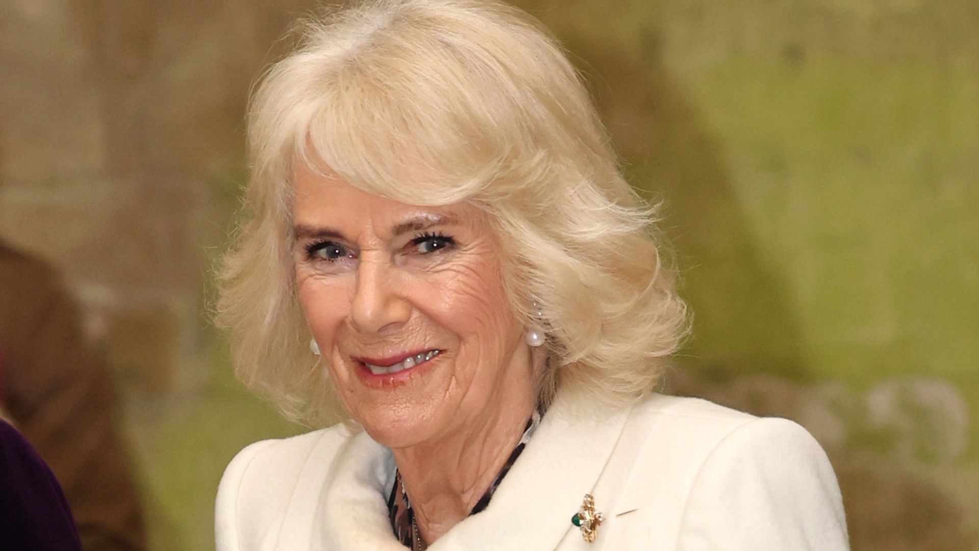 A close up photo of Queen Camilla in a white coat 
