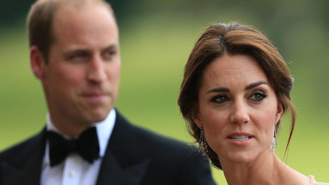 Prince William in a suit looking tense behind Princess Kate