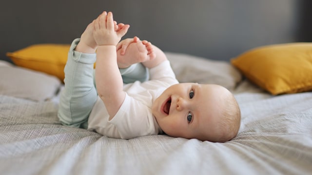 A 6 month old baby boy smiling, laying on a bed