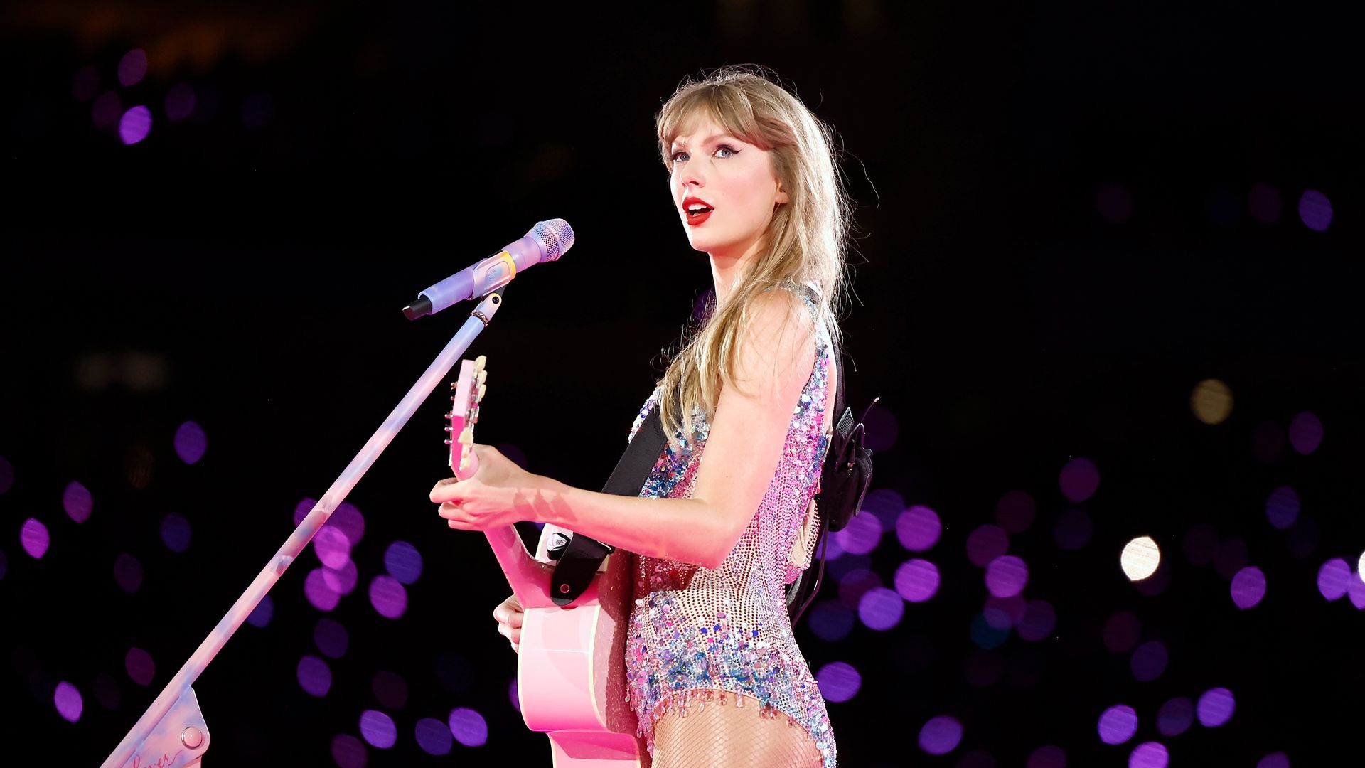 Taylor Swift playing guitar on stage in a glittering bodysuit