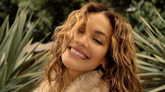 Rita Ora smiles to camera in a garden setting 