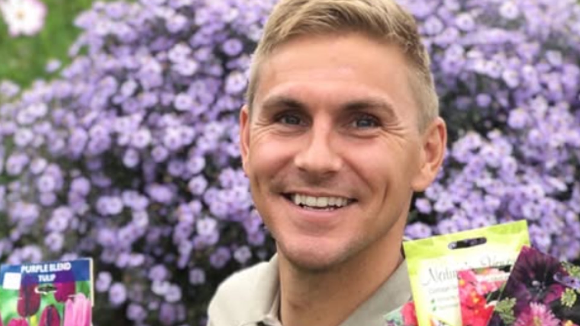 man holding up seed packets in garden