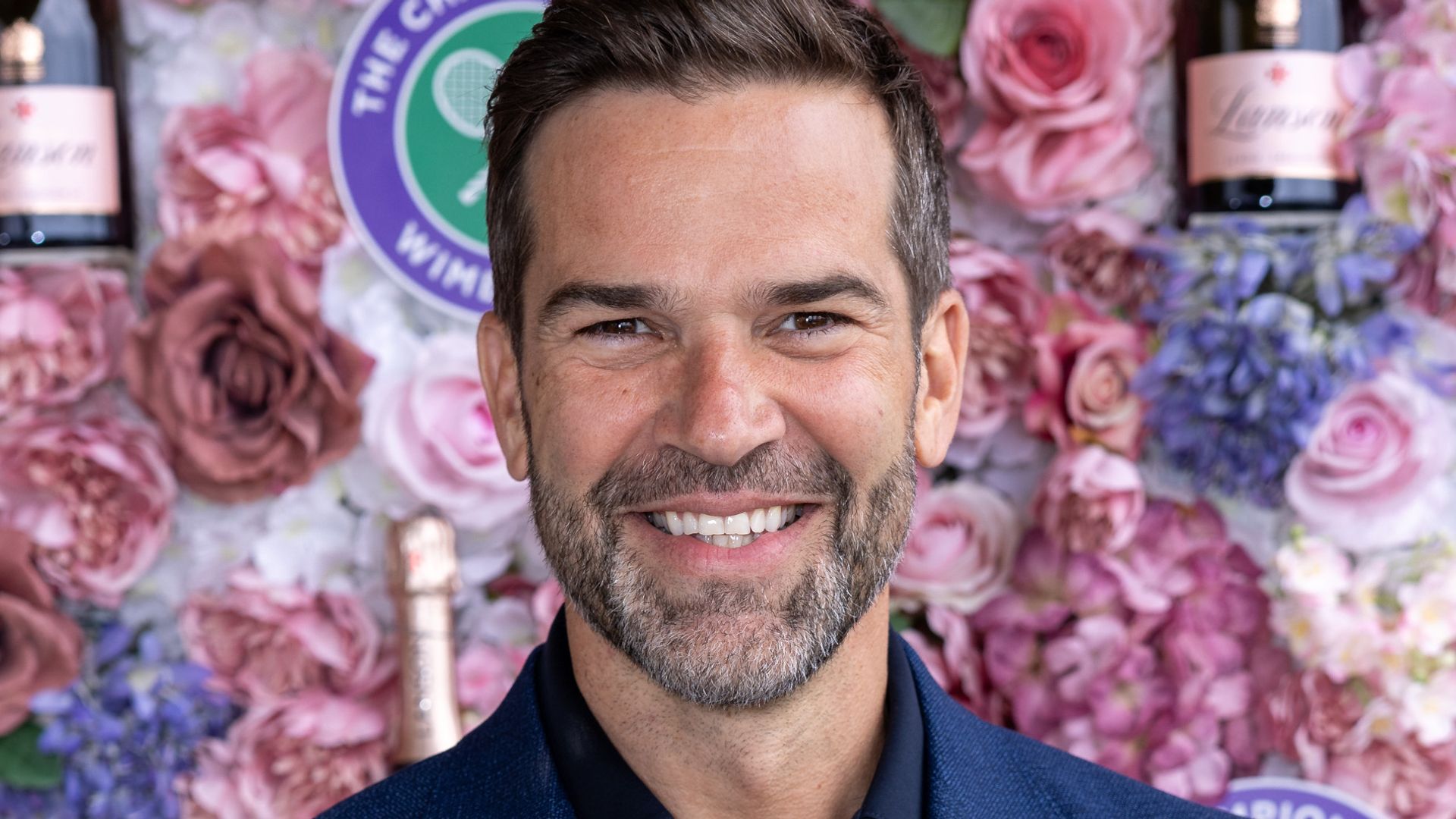 Gethin Jones in a blue suit against a pink floral wall