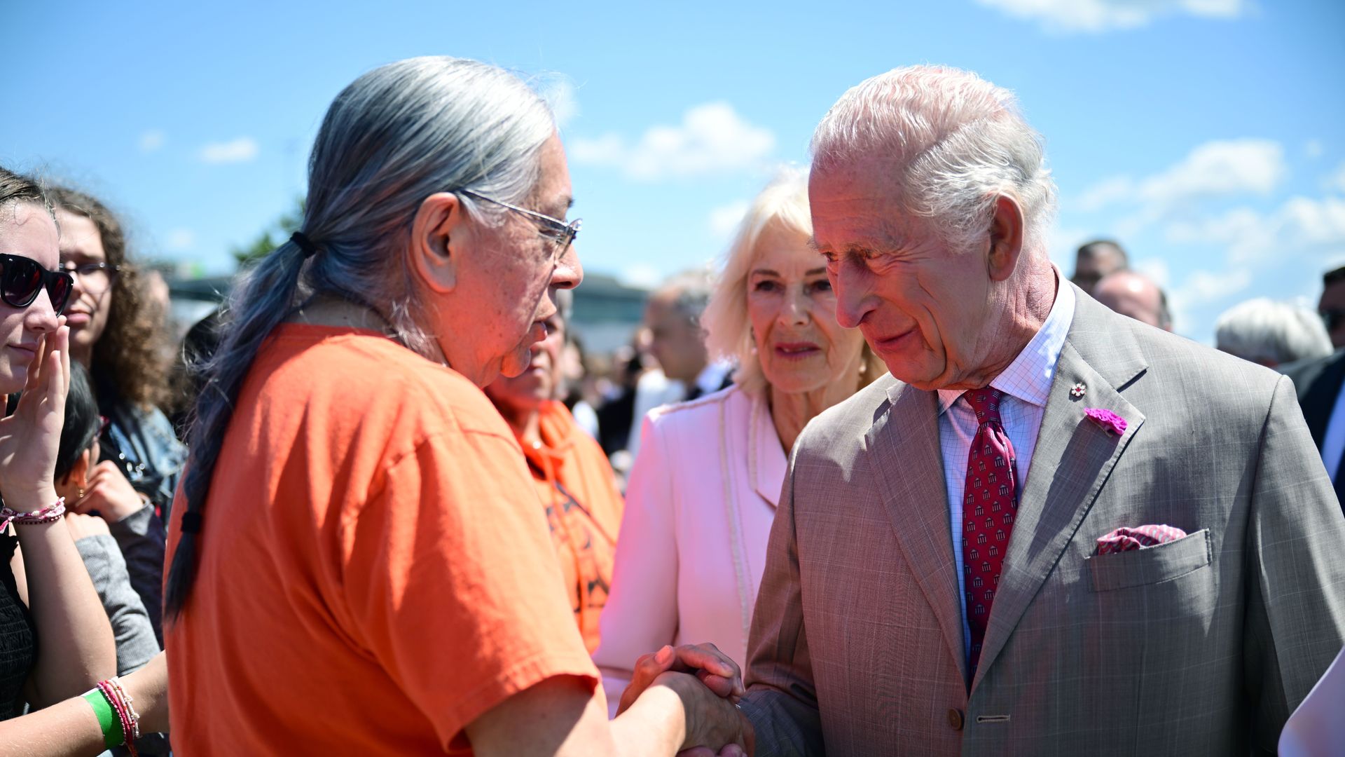 King Charles shaking hands with a man in an orange shirt