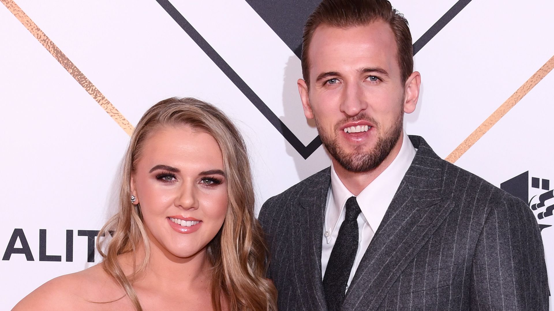 Harry Kane in a grey suit with his wife Kate in a black dress