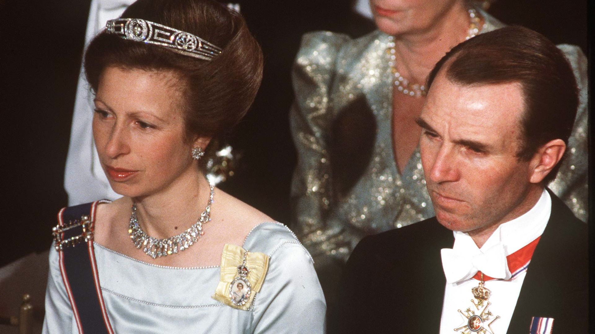 Princess Anne in a blue satin dress and tiara sitting next to her first husband Mark Phillips