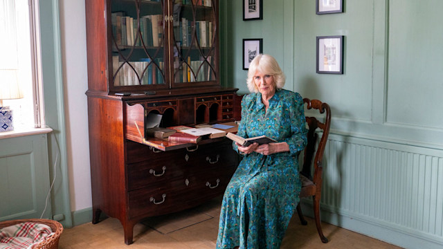 Queen Camilla in a green dress sitting on a chair reading a book