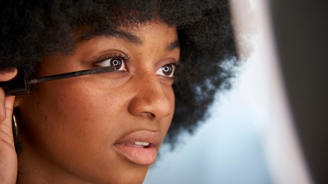 Close-up view of an Afro woman applying mascara on her eyelashes while doing her makeup. Concept of cosmetics, makeup and beauty.