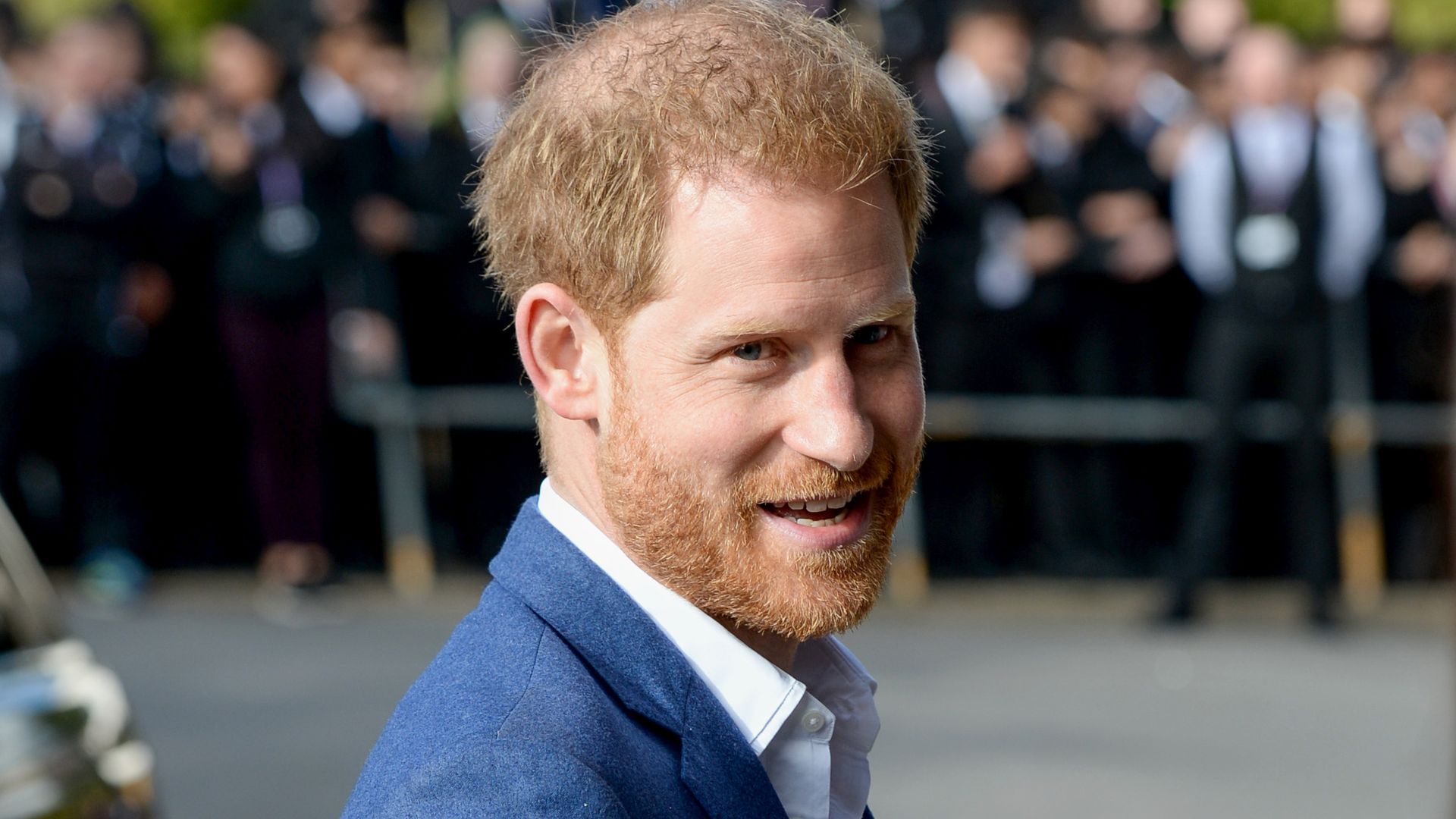 Prince Harry smiling in blue suit as he arrives at Nottingham school