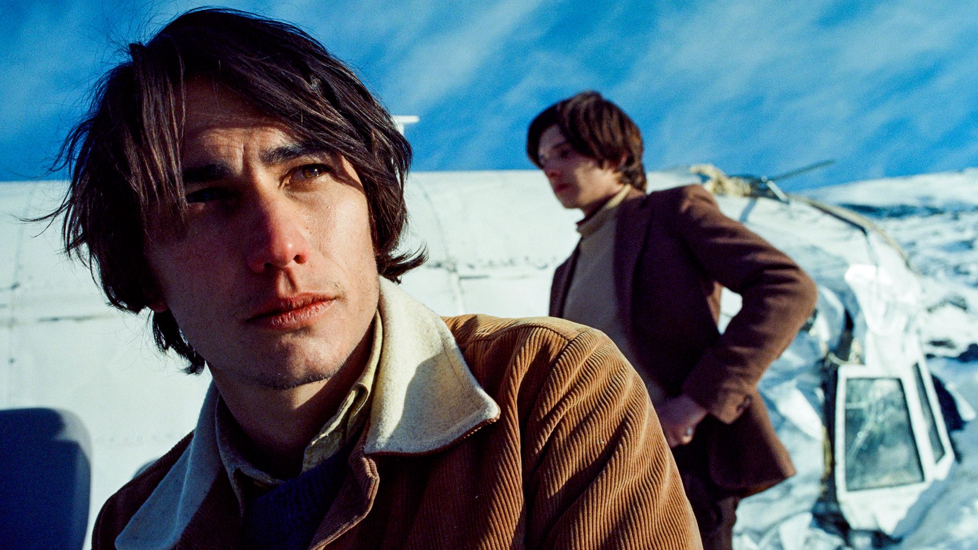 Two men stand outside of a plane crash in the Andes