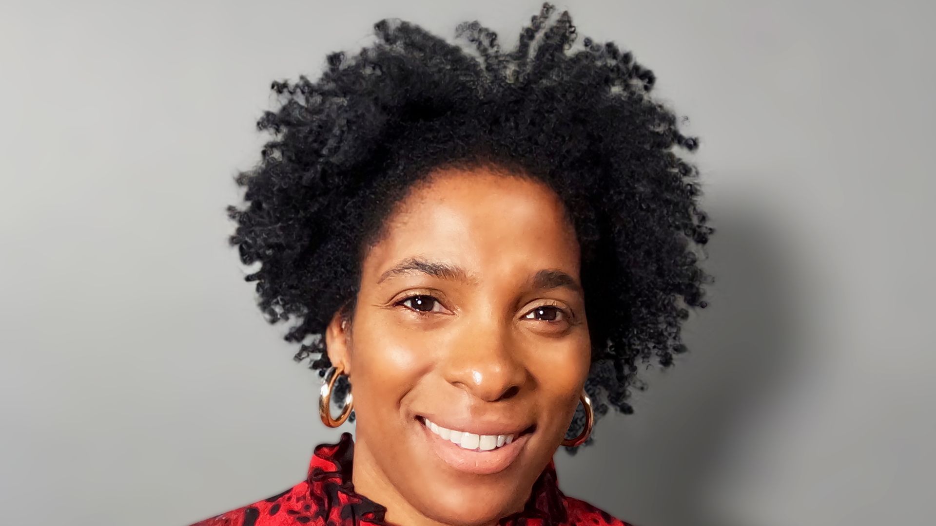 woman with an afro smiling wearing a red leopard print top
