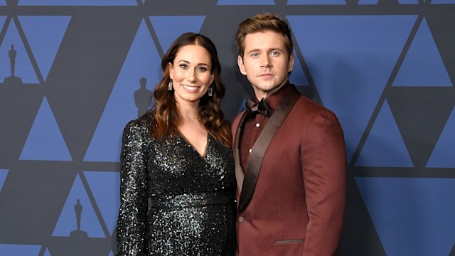 Woman in black dress and man in maroon suit posing on red carpet