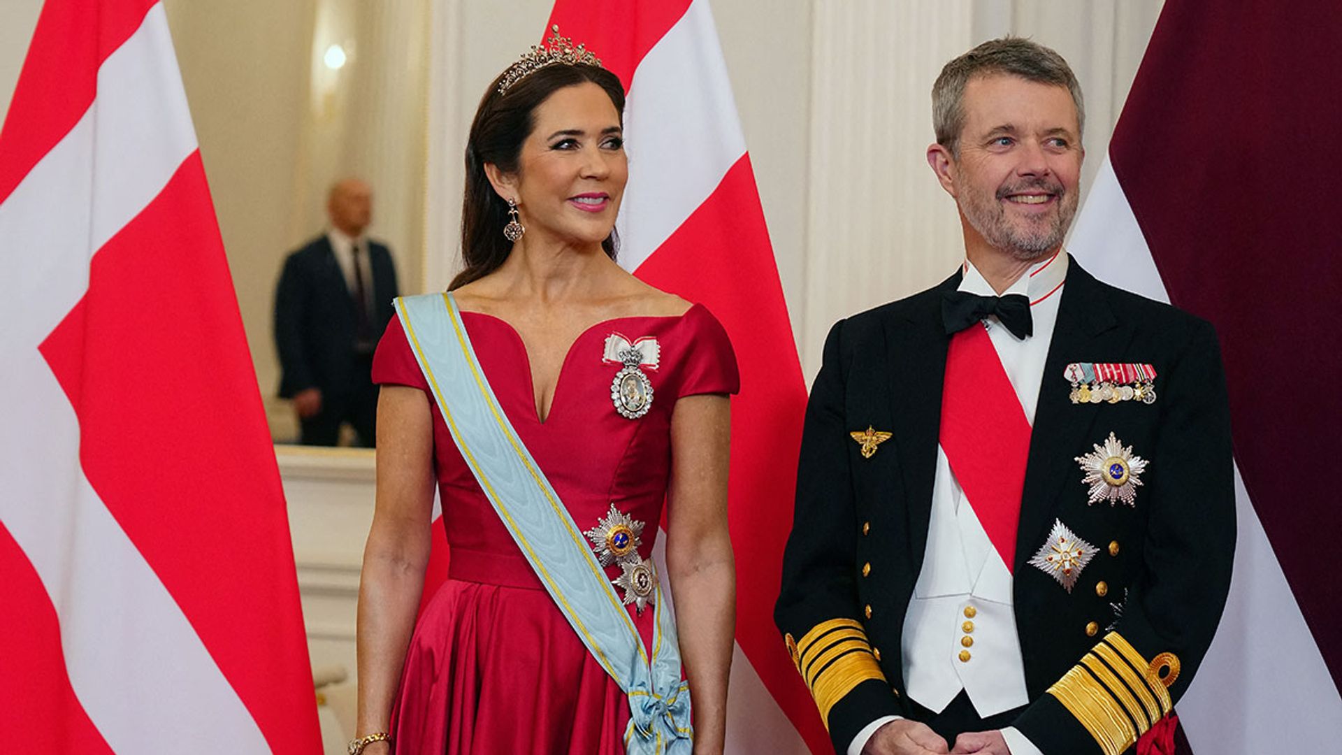 Queen Mary and King Frederik standing in front of flags at Latvia state banquet