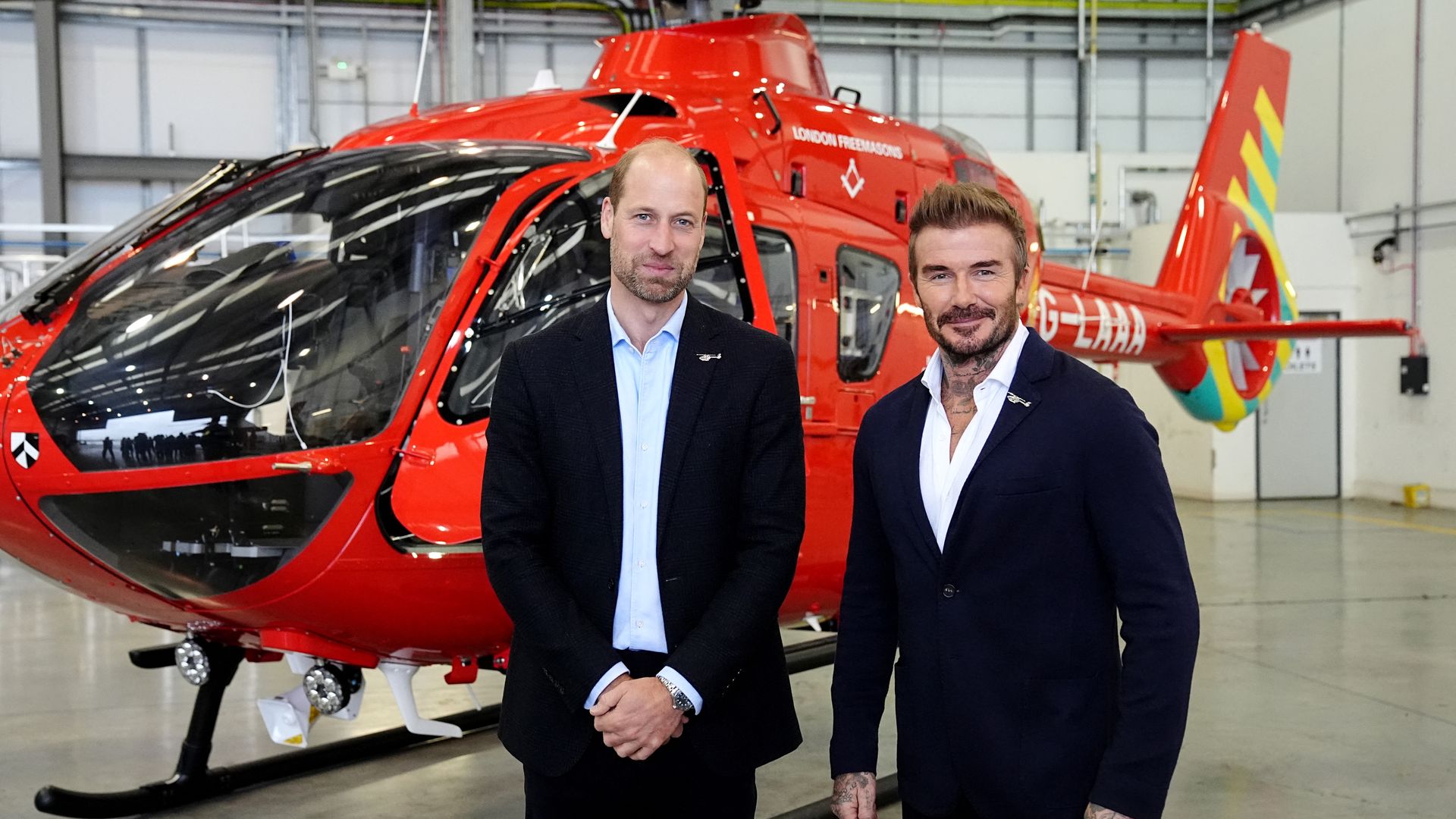 two men in suits standing in front of red helicopter