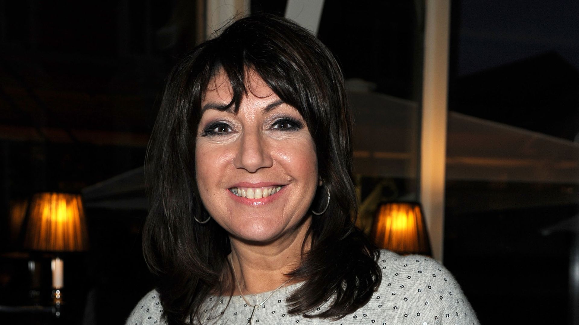 Jane McDonald in a white dress holding a glass of champagne