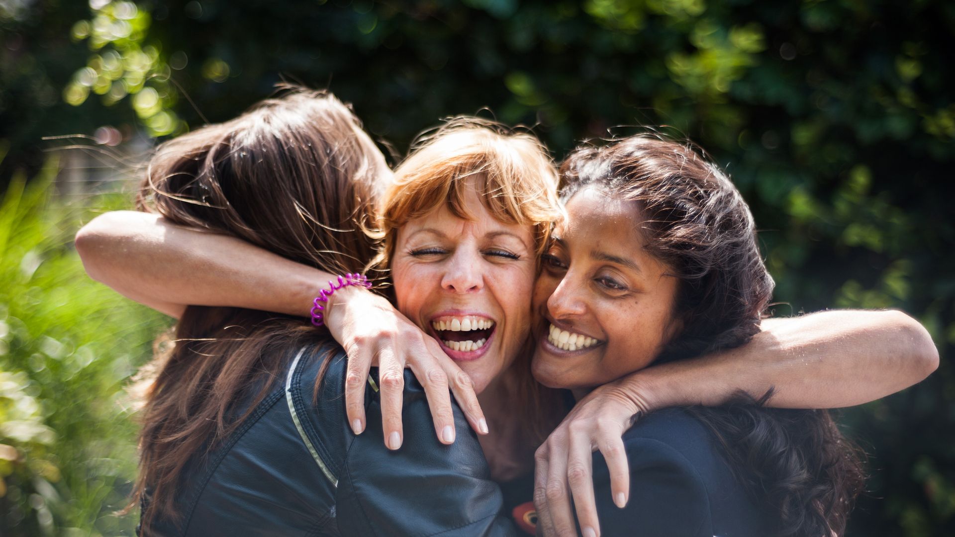 Three women, greeting and hugging outdoors.