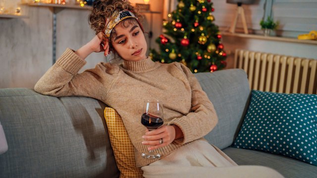 Young lonely woman drinking red wine during Christmas holiday