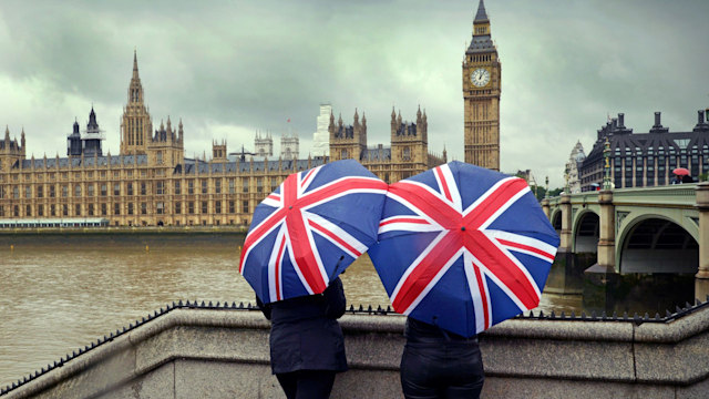 Tourists huddle beneath British flag umbrellas by houses of parliament