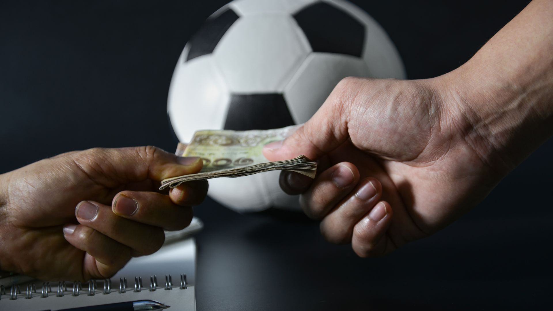 Two hands exchanging money in front of a football