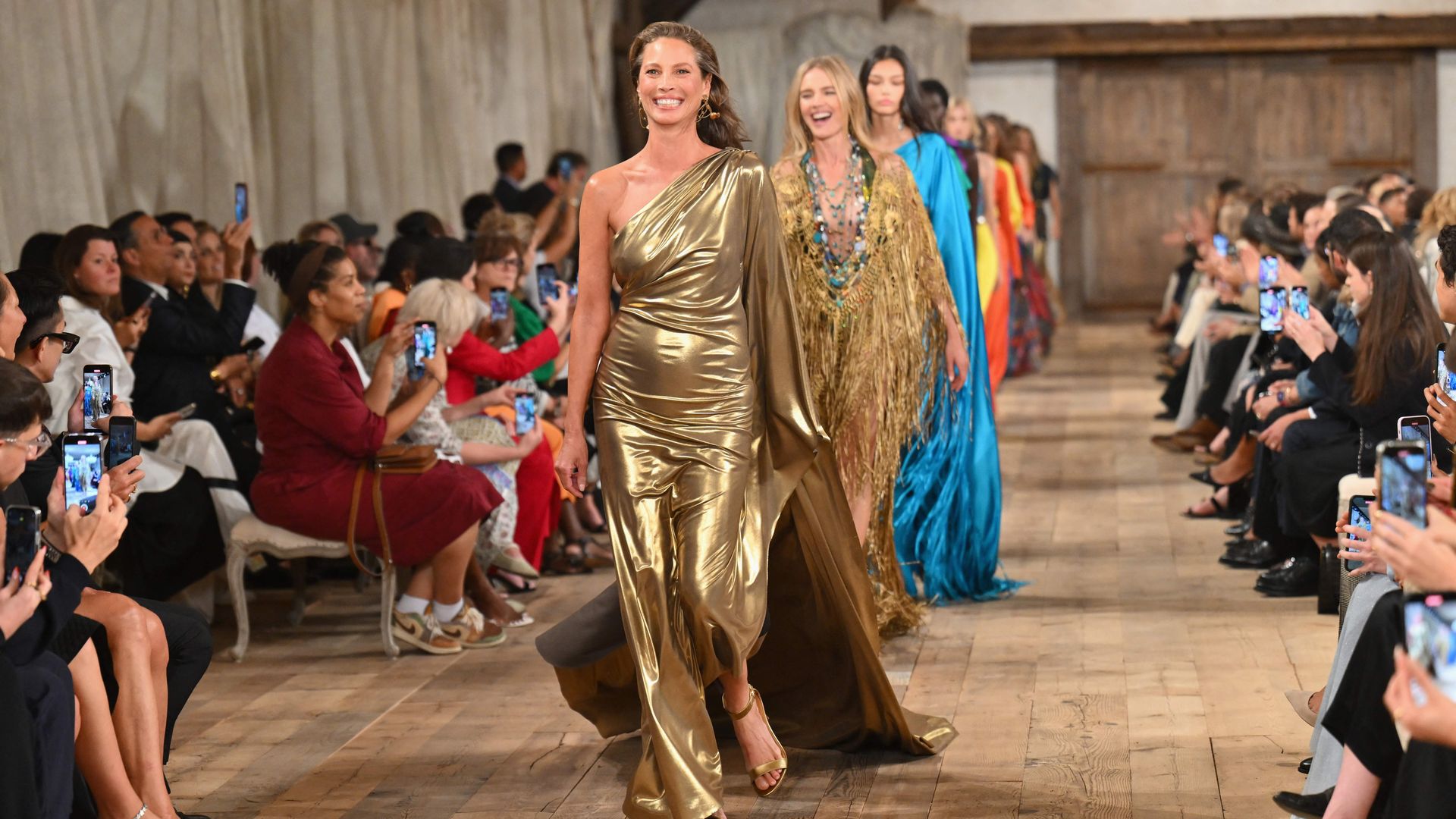 Christy Turlington walking in a gold one-shoulder dress 