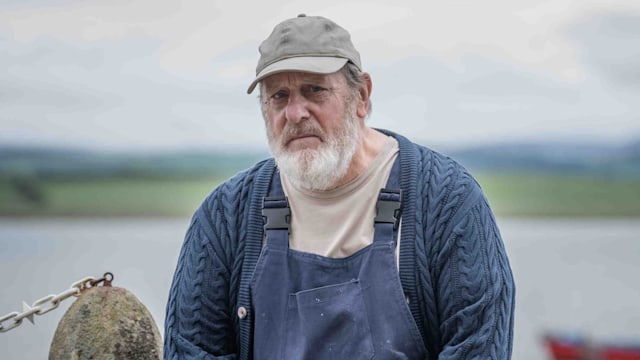 Man in fisherman's outfit sitting on dock