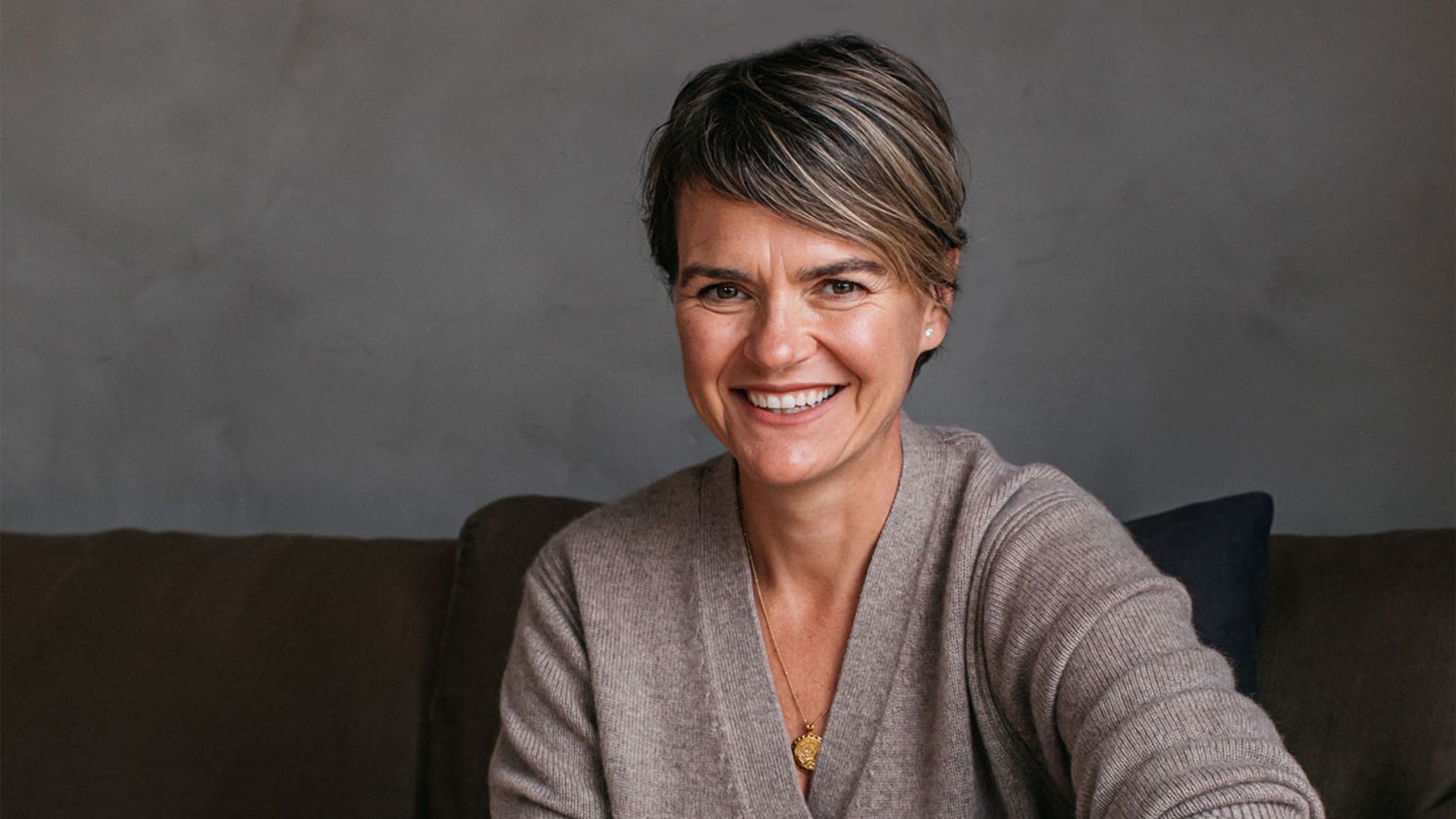 Short-haired smiling woman in a soft cardigan sitting on a sofa 