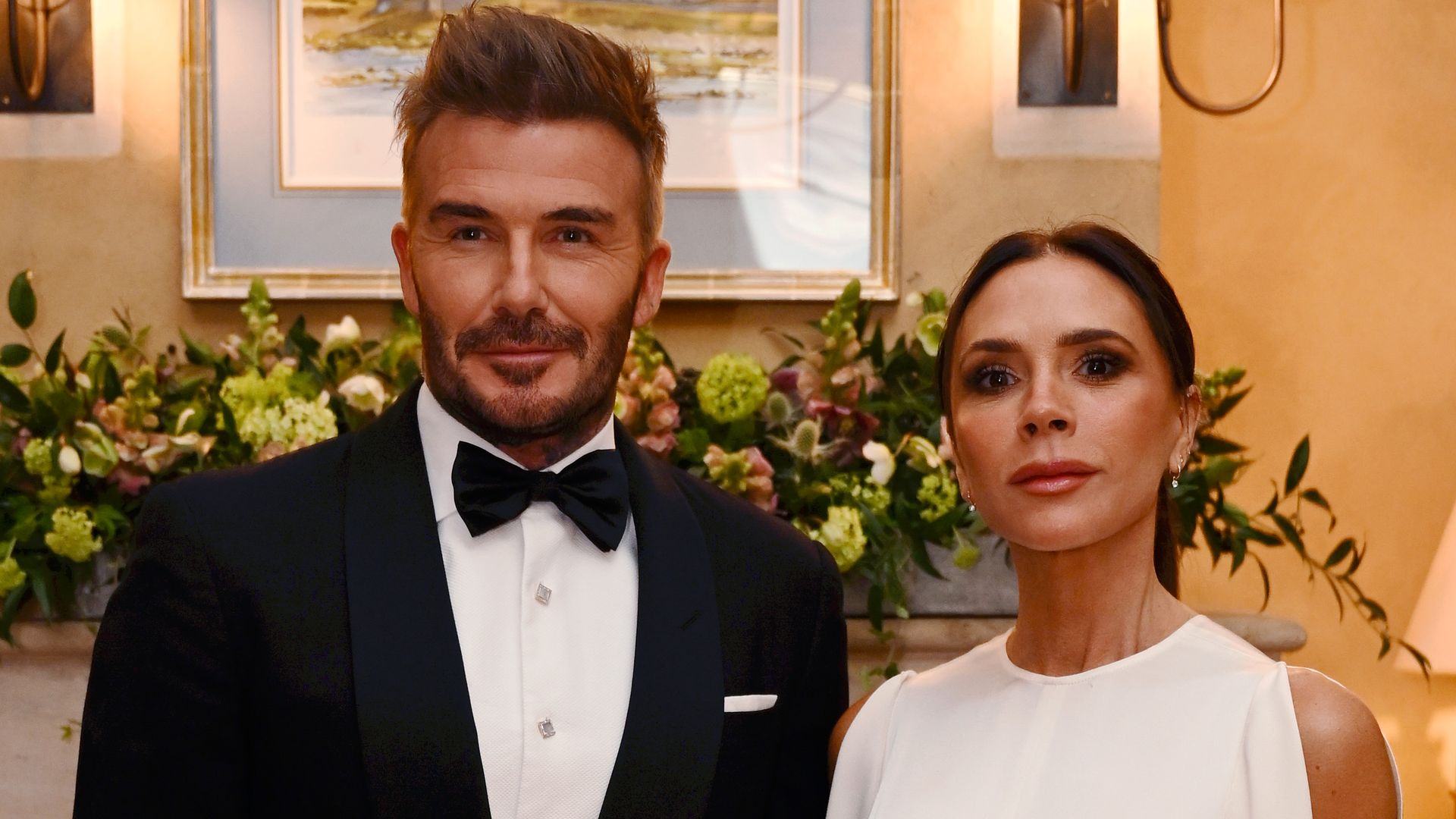 David Beckham in a tuxedo standing with Victoria Beckham in a white dress