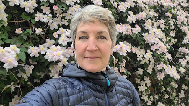 woman in a blue puffer jacket taking a selfie in front of pink flowers