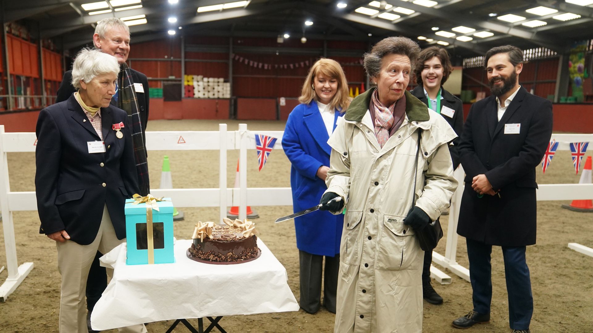 Princess Anne, wearing trench coat, cuts chocolate cake