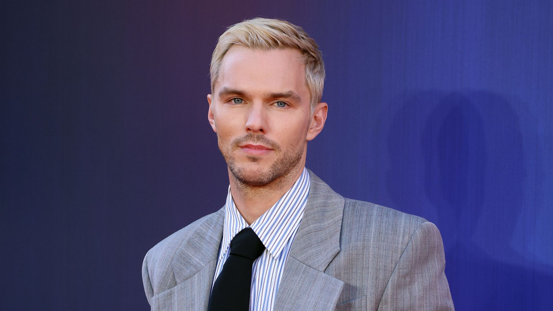 photo of nicholas hoult wearing grey suit and black tie with blonde hair