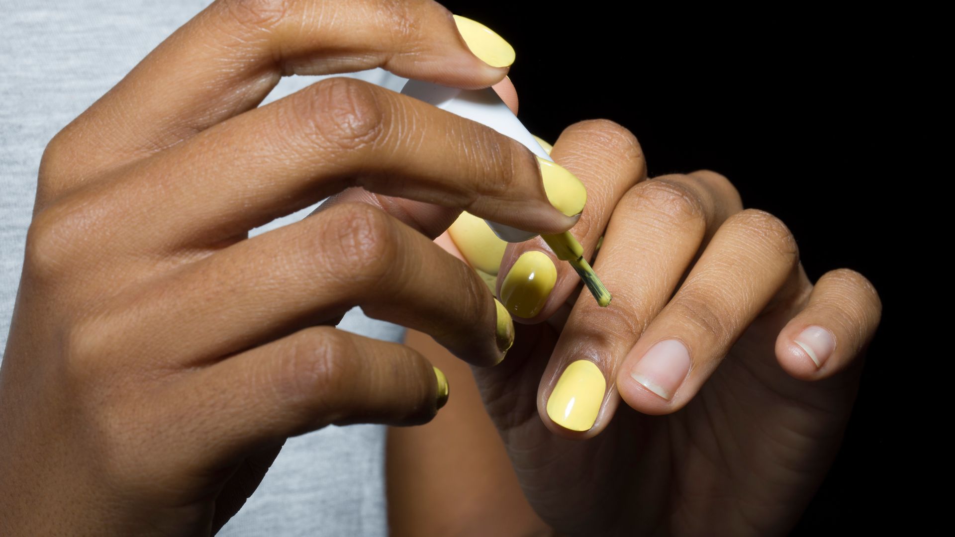Close-up of young mixed-race woman applying nail varnish,  with black background