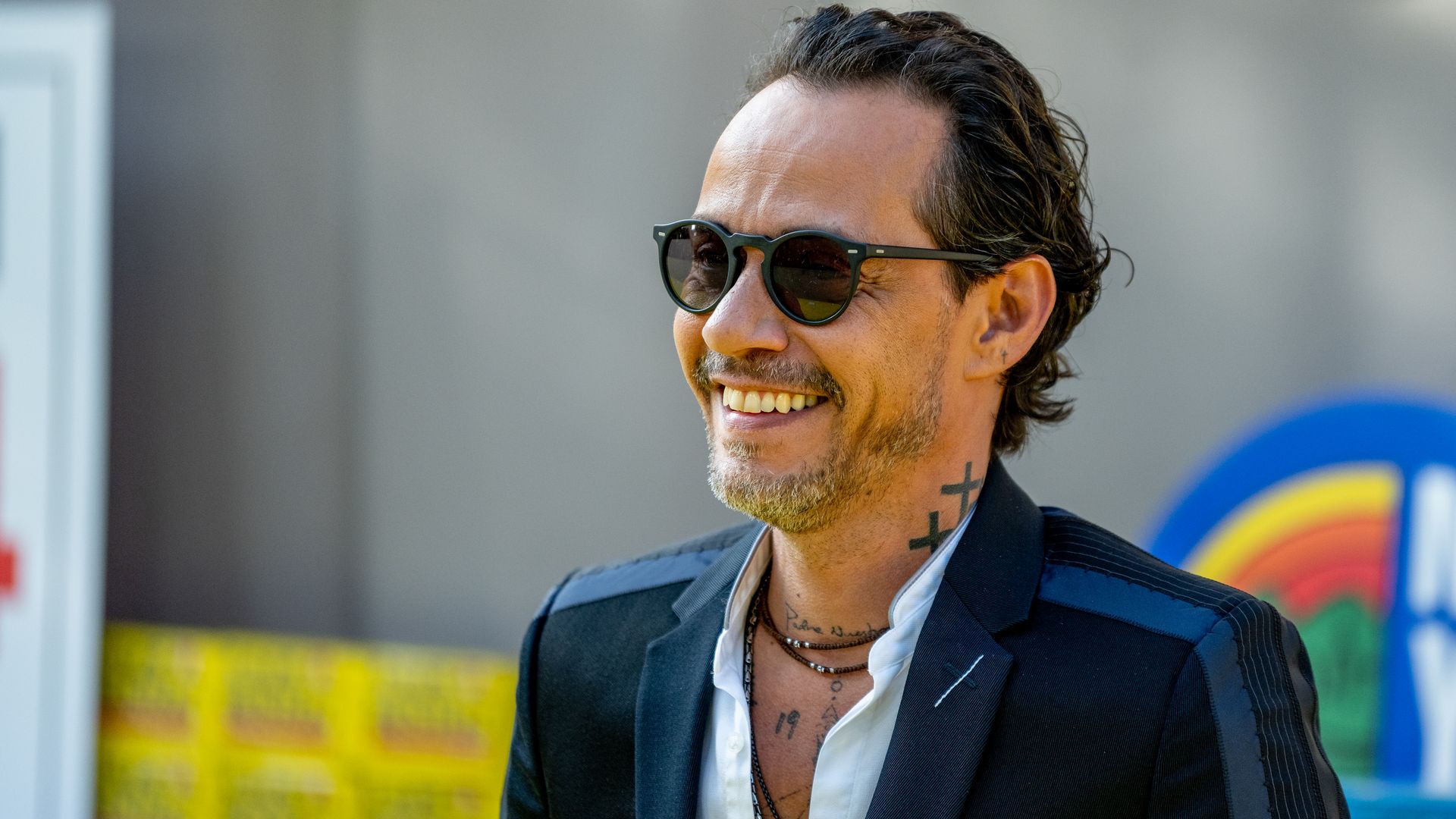 Marc Anthony smiling in glasses and a suit