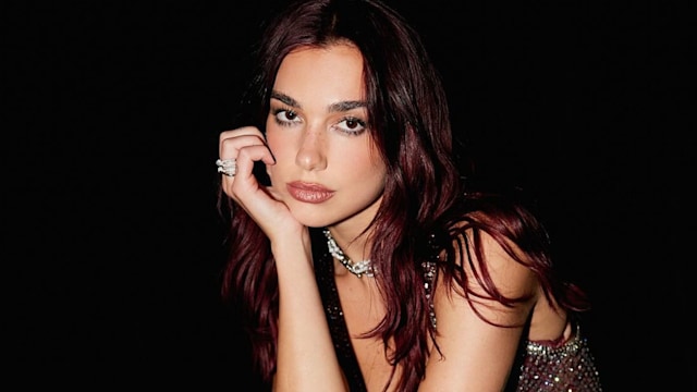 Dua Lipa poses in a sparkly burgundy outfit backstage