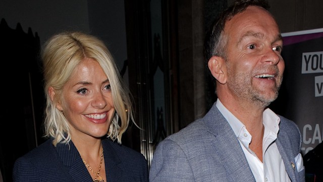 Holly Willoughby and Dan Baldwin in blue suits linking arms as they leave Claridge's Hotel in 2019