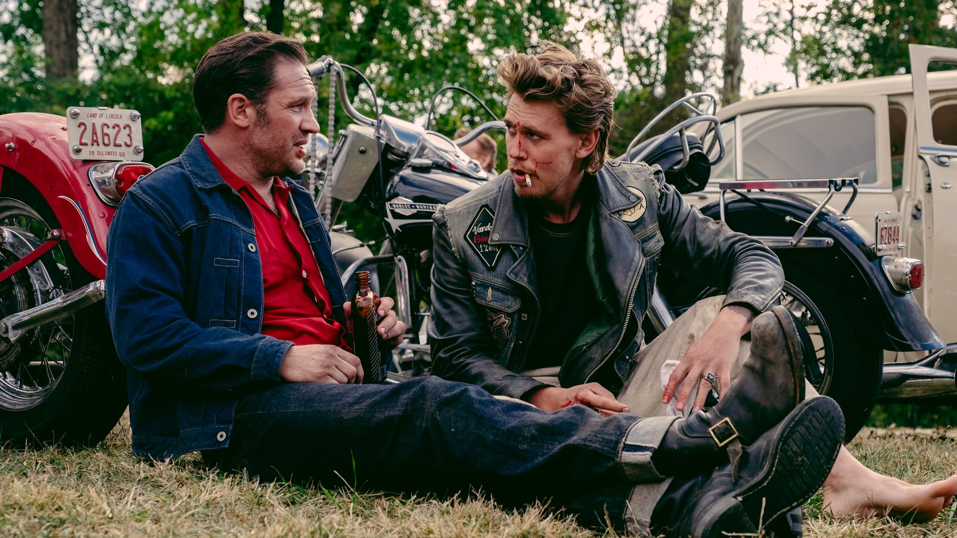 two men sitting on grass next to motorbikes