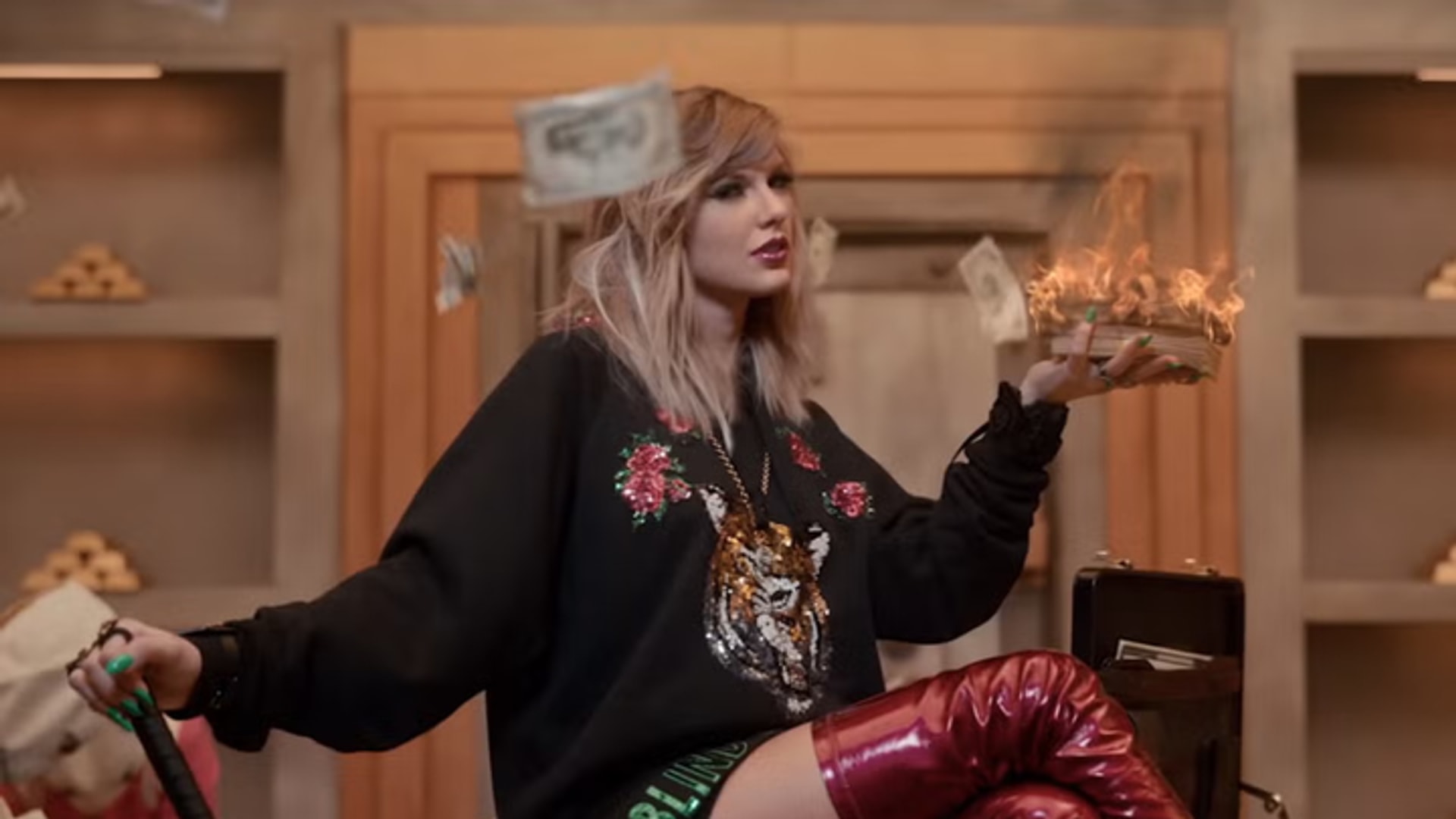 Taylor Swift sits on a desk and holds a baseball bat in still from Look What You Made Me Do