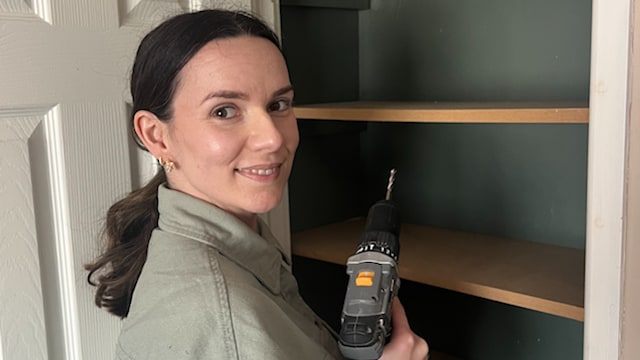 woman with drill by shelves inside cupboard 