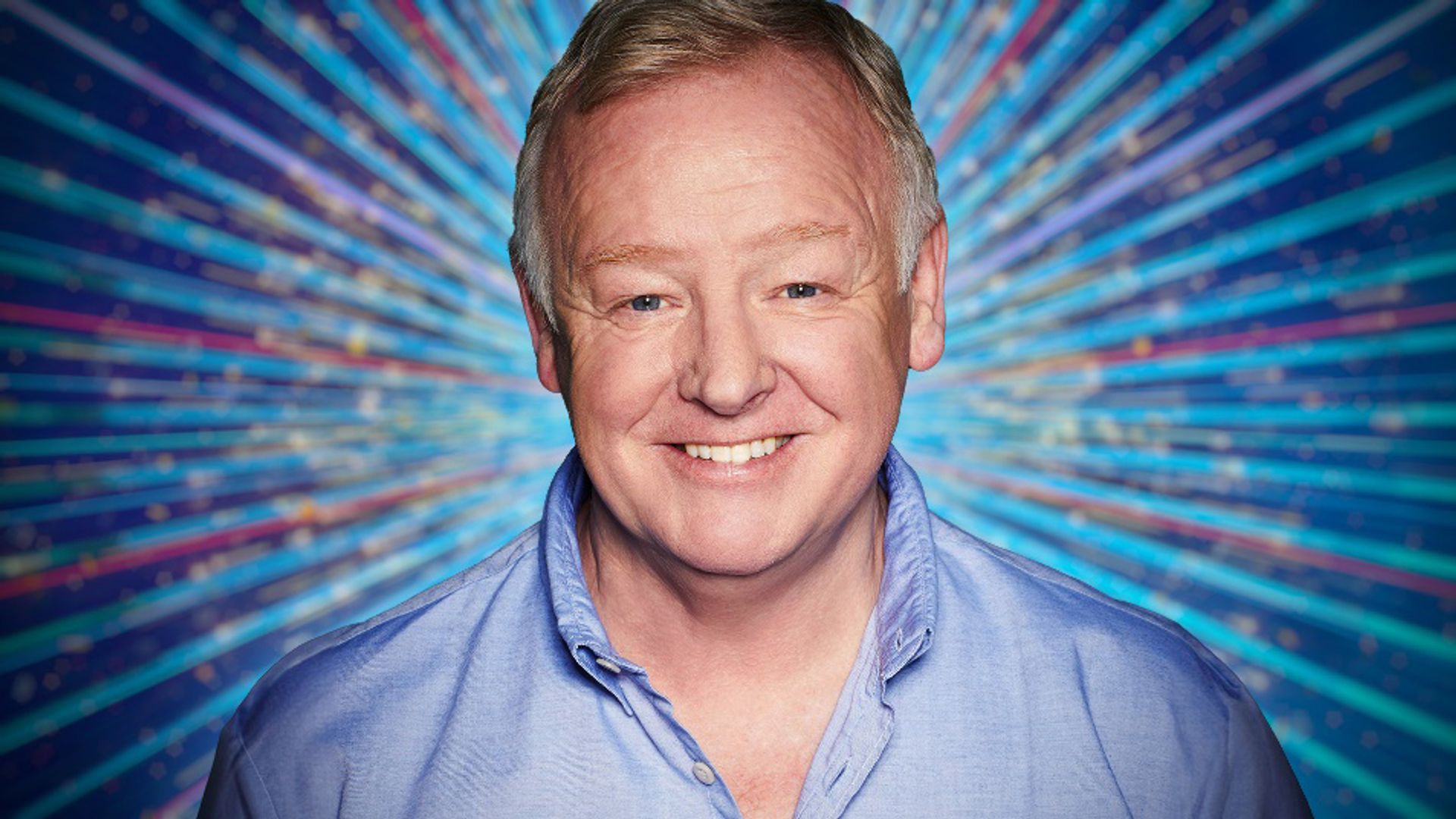 Close up of Les Dennis smiling with the Strictly background