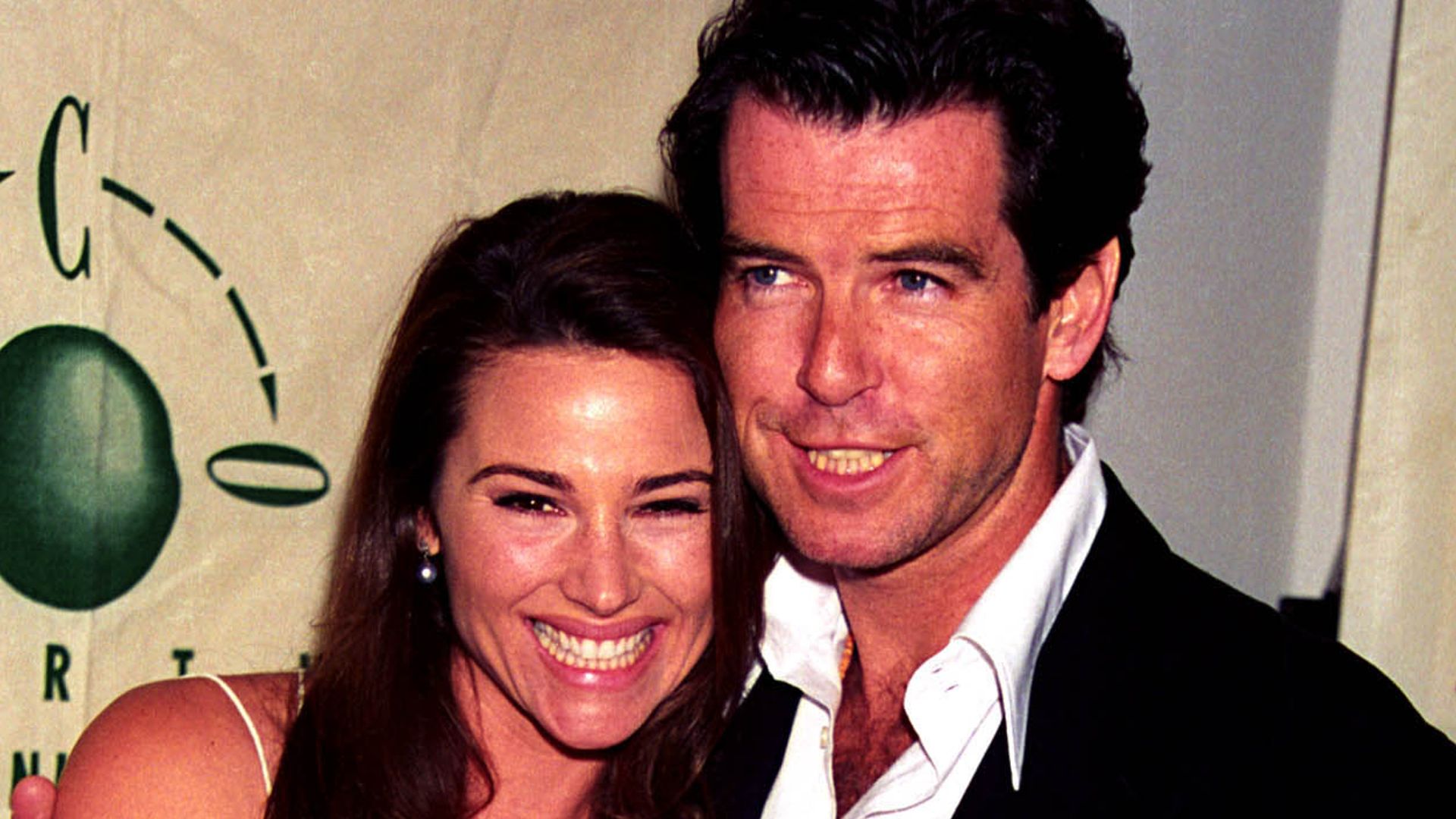 Keely Shaye Smith grinning in a white dress and Pierce Brosnan in a suit