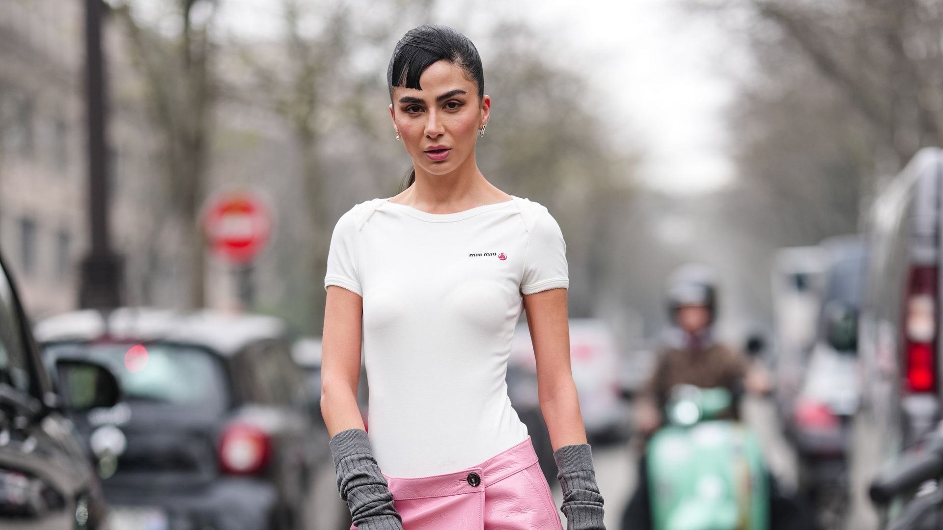  A guest wears silver earrings, white short sleeve Miu Miu shirt, dark gray fingerless Miu Miu gloves, shiny dark pink MIu Miu leather midi skirt, shiny black Miu Miu leather bag, dark brown tights, shiny dark green pointed toe sling back heels leather shoes, outside Miu Miu, during the Paris Fashion week Women's Fall/Winter 2025-2026 on March 11, 2025 in Paris, France