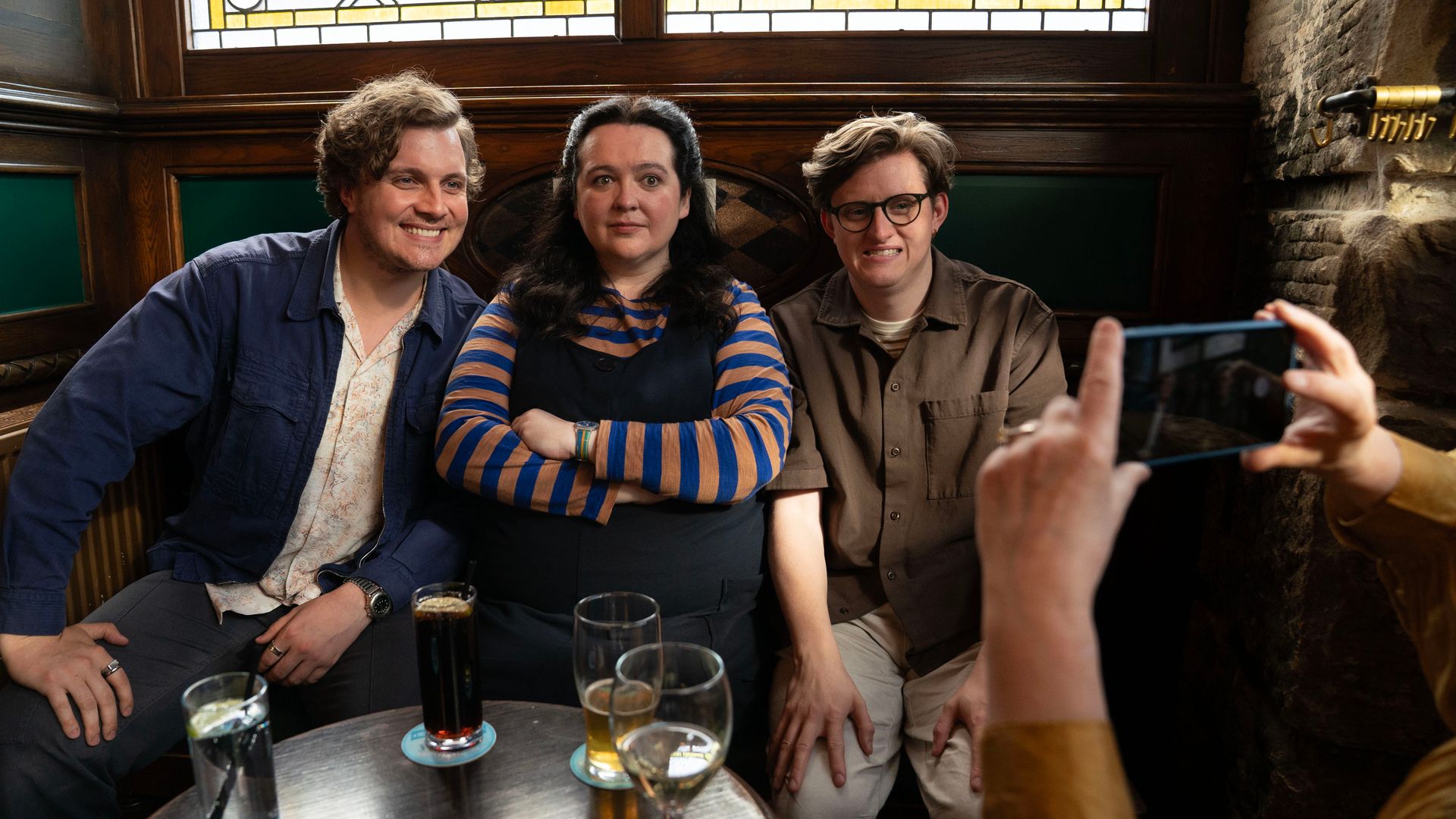 Still image of Hyoie O'Grady, Ashley Storrie and Lorn Macdonald sitting in a pub in Dinosaur