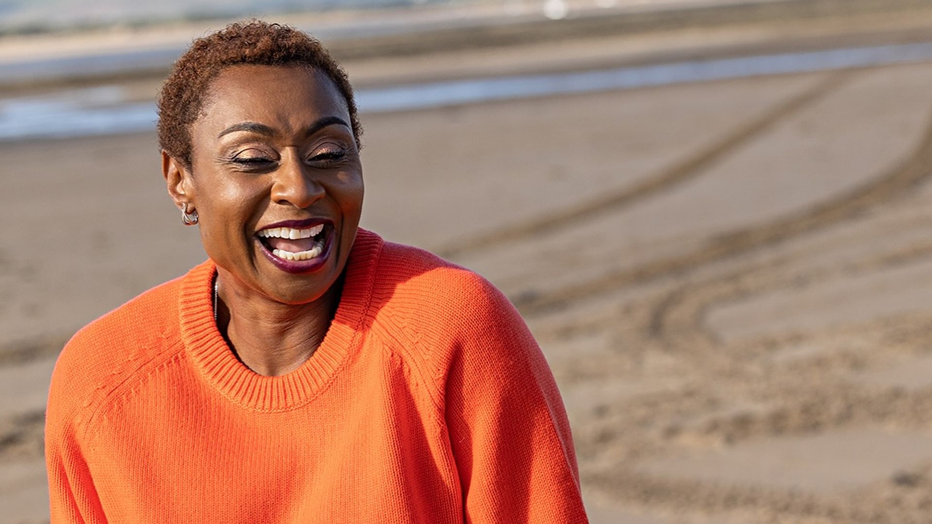 Michelle Griffith smiling on the beach in an orange jumper
