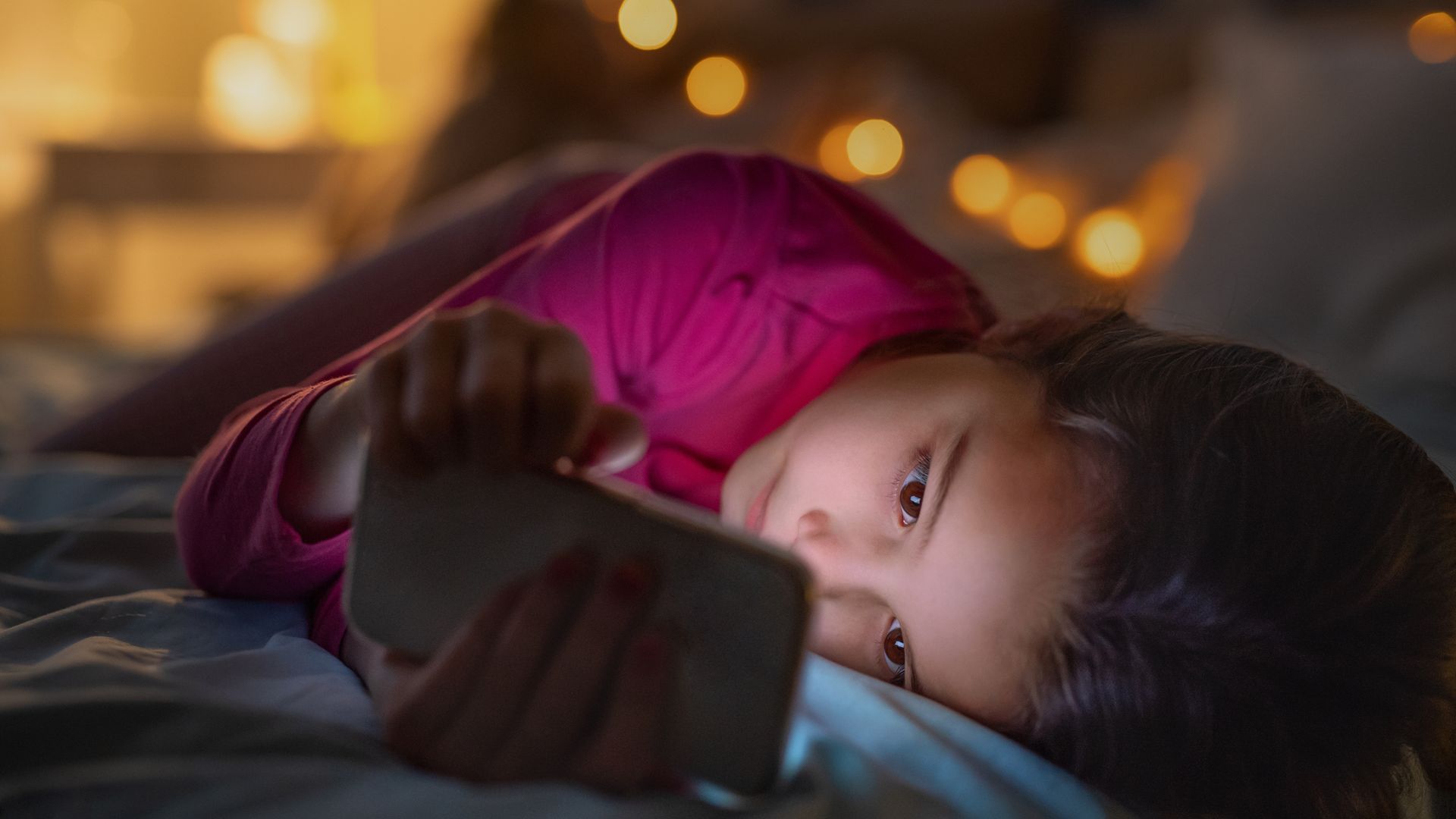 Small girl indoors on bed at night, using telephone.