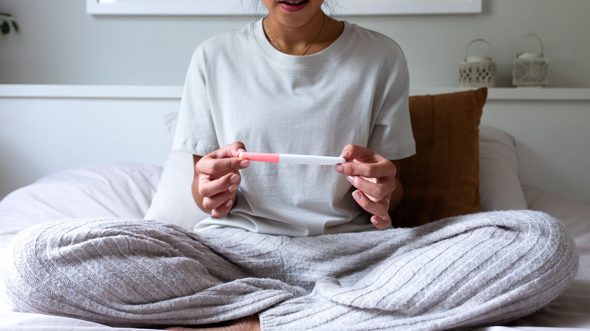 Unrecognizable young woman disappointed to see negative pregnancy test in bedroom. Young female worried after checking positive pregnancy test. Pregnancy.