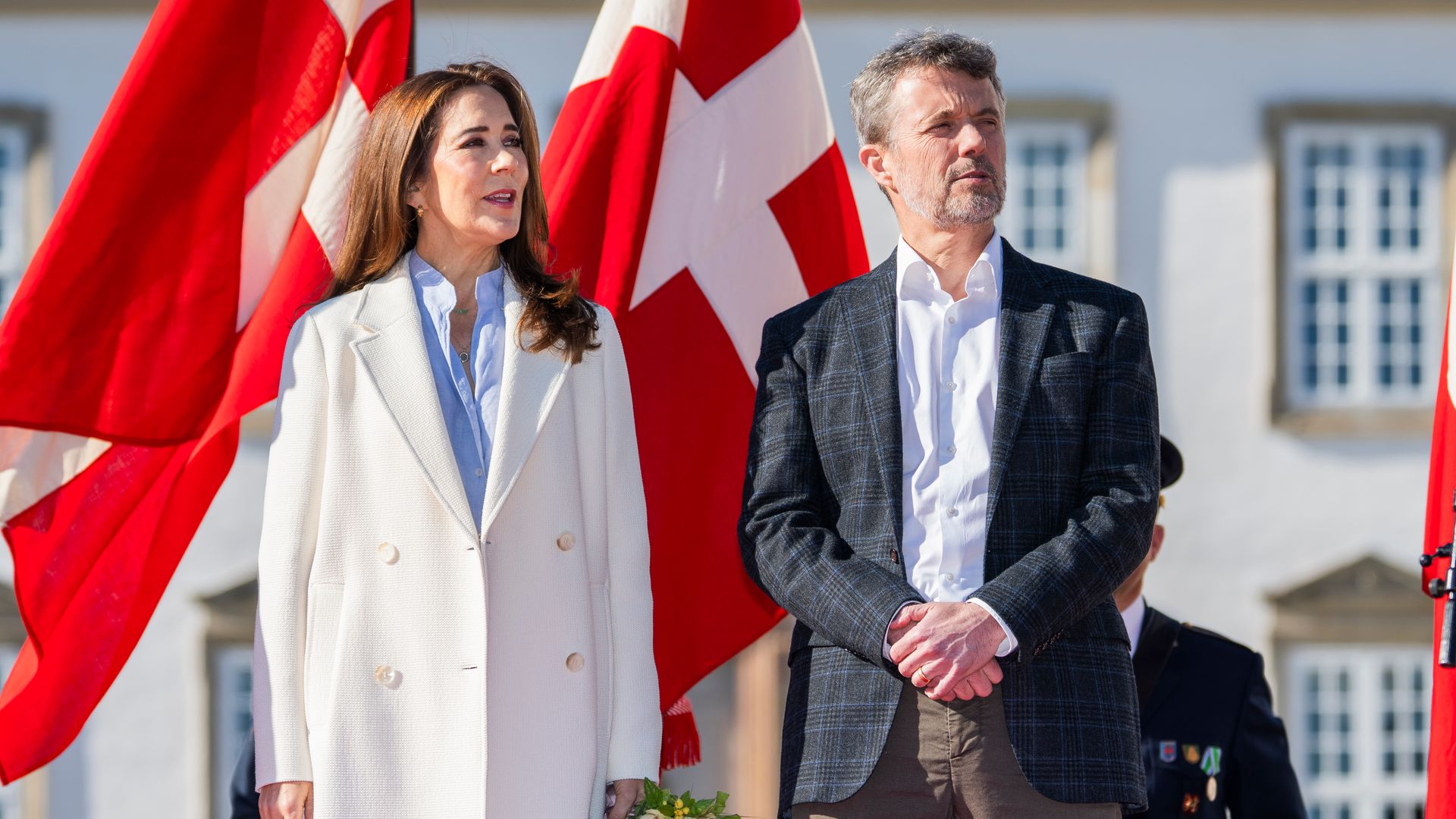 Frederik and Mary standing in front of Danish flag