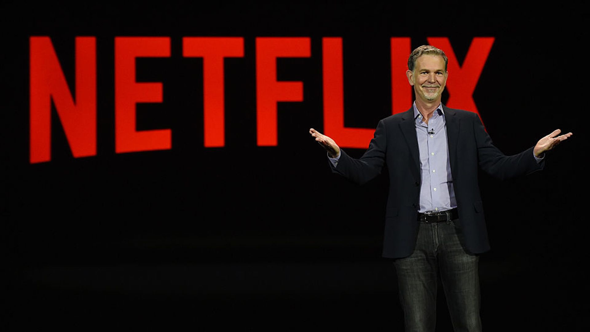 Reed Hastings standing in front of the Netflix logo. 